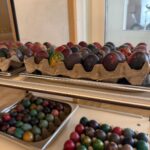 Več pladnjev pisanih pirhov je razstavljenih na vozičku, kjer so lepo zloženi in pripravljeni za ogled.