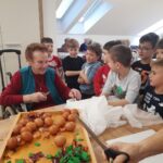 Otroci in starejši skupaj sodelujejo pri barvanju pirhov, kar ustvarja lepo medgeneracijsko povezanost.