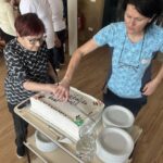 Dve ženski režeta rojstnodnevno torto na vozičku, pripravljeno za razdelitev med prisotne.