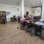 Mladi harmonikar igra prijetne melodije, medtem ko stanovalci ob mizah uživajo v prazničnem programu in druženju.