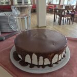Na mizi je okusna rojstnodnevna torta s čokoladnim prelivom, pripravljena za praznovanje aprilskih rojstnih dni.