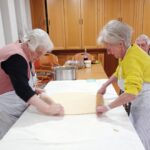 S skupnimi močmi valjajo testo za potico, pri čemer se prepletata izkušnje in sodelovanje.