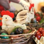 Velikonočna dekoracija z lesenimi kokoškami v košarici, obkrožena z barvanimi pirhi.