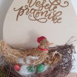 Velikonočna dekoracija s kokoško v gnezdu in pirhi ter napisom Vesele praznike pričara praznično vzdušje.