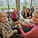 Skupina stanovalk sedi okoli mize in sodeluje pri ustvarjanju pirhov, ob tem pa prijetno klepetajo in sodelujejo.