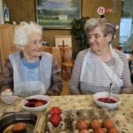 Dve stanovalke z nasmehom barvata pirhe v rdeči barvi in uživata v skupnem ustvarjanju.