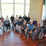 Skupina oseb sedi v krogu v večnamenskem prostoru in sodeluje pri skupnem dogodku.