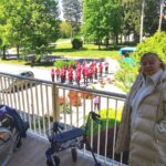 Stanovalci stojijo na balkonu doma in poslušajo godbo, ki igra pred stavbo.