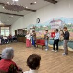 Mladi glasbeniki in igralci nastopajo na kulturnem dogodku v domu za starejše.
