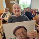 Stanovalec doma za starejše drži gramofonsko ploščo med glasbeno dejavnostjo s starimi uspešnicami.