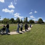Skupina obiskovalcev hodi po tlakovani poti skozi park, ena oseba potiska invalidski voziček.