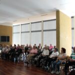 Stanovalci v skupnem prostoru poslušajo glasbeni nastop ob klavirski spremljavi.