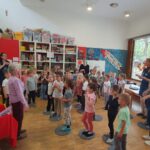 Otroci in stanovalka doma za starejše sodelujejo pri gibalni dejavnosti v vrtcu.