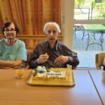 Stanovalci sedijo za mizo, pred njimi je rojstnodnevna torta z napisom »Vse najboljše 93 let«.