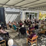 Udeleženci skupinske vadbe sedijo v krogu na zunanji terasi doma za starejše.