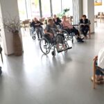 Skupina stanovalcev sedi v krogu v večnamenskem prostoru, oseba na stolu pa govori v mikrofon.
