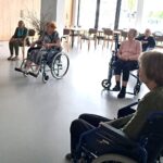 Skupina stanovalcev sedi v krogu v večnamenskem prostoru in spremlja dogajanje.