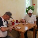 Stanovalca uživata v pokušini sveže pečenega češnjevega štrudlja. Ob sladici in druženju vlada zadovoljno in sproščeno vzdušje.