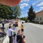 Skupina ljudi ob cesti maha s slovenskimi zastavami, medtem ko mimo peljejo kolesarji.