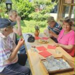 Stanovalci po nabiranju zelišč sedijo za mizo na prostem in se družijo ob osvežitvi.
