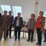 Skupina starejših pevk in pevcev stoji v skupnem prostoru doma ter skupaj prepeva pred občinstvom.