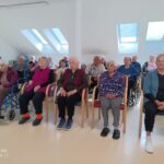 Stanovalci sedijo v prvih vrstah in pozorno poslušajo pevski nastop v skupnem prostoru doma.