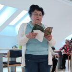 Članica pevskega zbora stoji pred občinstvom in bere besedilo iz knjižice med kulturnim nastopom.