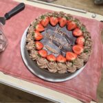 Torta z jagodami in napisom »Vse najboljše« je pripravljena na vozičku ob krožnikih in kozarcih.