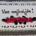 Torta z napisom »Vse najboljše!« in okrasom iz rožnatih cvetov.