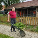 Stanovalec prevaža samokolnico, polno zelenega vrtnega odpada, proti zbirnemu mestu.
