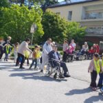 Otroci iz vrtca in stanovalci doma starejših skupaj sodelujejo na sprehodu po okolici doma v okviru medgeneracijskega dogodka.