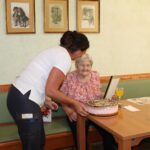 : Oskrbovalka nese torto k stanovalki ob praznovanju 90. rojstnega dne.