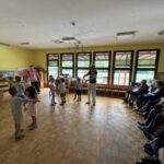 troci stojijo v krogu, stanovalci sedijo ob strani v sobi.