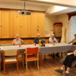 Skupina stanovalcev sedi za mizo z pijačami in kozarci v sobi.
