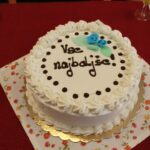 Bela torta z napisom „Vse najboljše!“ na rdeči mizi.