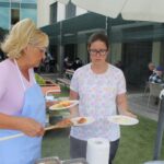 Dve ženski s predpasniki postrežeta krožnike s hrano na zunanji terasi.