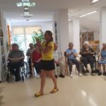 Ženska stoji pred sedečo skupino ljudi in ploska z rokami.