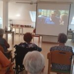 Skupina ljudi sedi in spremlja film na projekcijskem platnu.