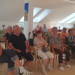 Skupina ljudi sedi v vrstah in je obrnjena proti projekcijskemu platnu.