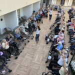 Skupina stanovalcev sedi na terasi in dviguje roke med vadbo.