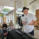 Ivan Švajgl v črnem klobuku govori v mikrofon pred občinstvom.
