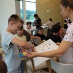 Otrok izbira barvo s palete, medtem ko oseba ob njem drži papir z barvnimi odtisi.