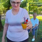 Ženska na vrtu drži kozarec oranžne pijače, okrašen z jagodo in borovnicama.