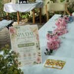 Miza je pripravljena za SPA dan z napisom »SPA day za naše dame«, cvetjem, svečami in izdelki za nego.