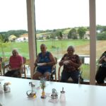Skupina žensk sedi ob velikih oknih in je iz skledic.