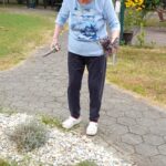 Ženska na vrtu s škarjami reže sivko in v roki drži šopek.
