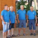 Štirje moški v modrih majicah stojijo drug ob drugem in pojejo.