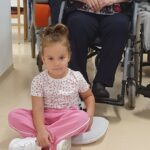 Otrok sedi na tleh pred žensko na invalidskem vozičku.