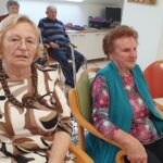 Dve ženski sedita v ospredju, za njima sedi več oseb.