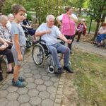 Oseba na invalidskem vozičku drži rdeč lok, ob njej stojita otrok in druga oseba.